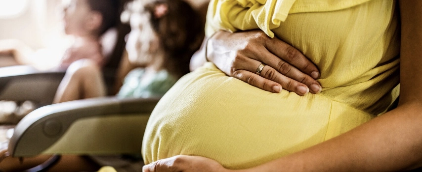 Pregnant woman, who did some research on travel insurance for pregnancy before her trip, travelling on plane with children