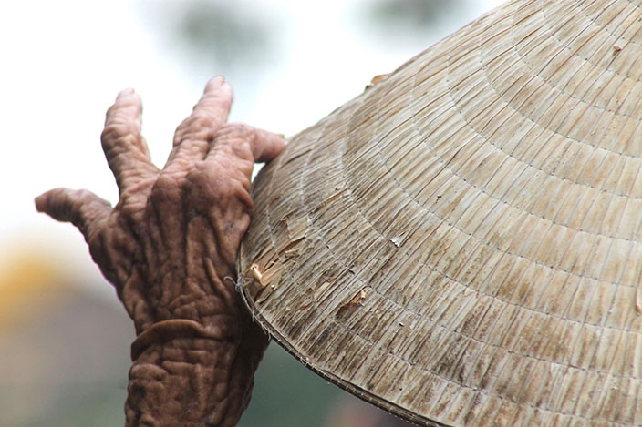 Cover-More New Zealand Facebook photo competition winner: Old woman adjusting her woven hat at a river bank in Vietnam