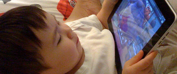 A child lays down and watches a video on an iPad